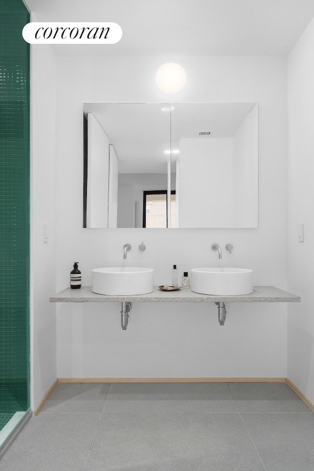 full bath with visible vents, baseboards, tiled shower, dual sinks, and tile patterned floors