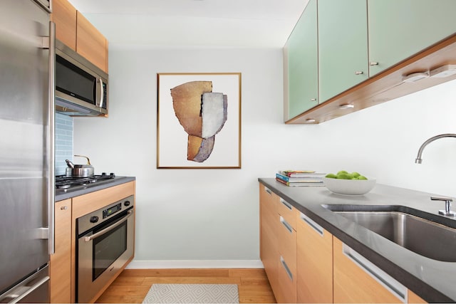 kitchen featuring stainless steel appliances, light wood finished floors, dark countertops, and a sink