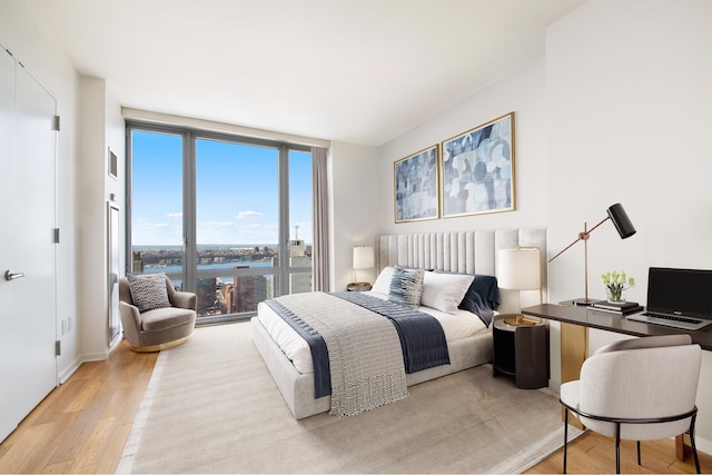 bedroom with light wood-type flooring, a water view, baseboards, and a wall of windows