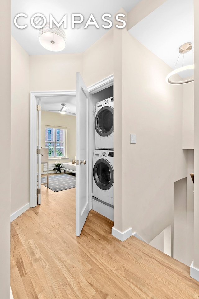 washroom with stacked washer / dryer, light wood-style flooring, laundry area, and baseboards