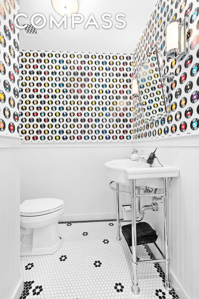 half bathroom with tile patterned floors, a wainscoted wall, and toilet