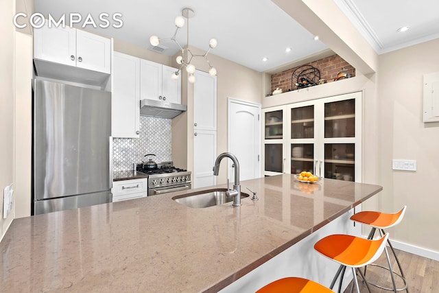 kitchen with a breakfast bar, a sink, stainless steel appliances, under cabinet range hood, and tasteful backsplash