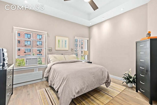 bedroom featuring a tray ceiling, multiple windows, baseboards, and light wood finished floors