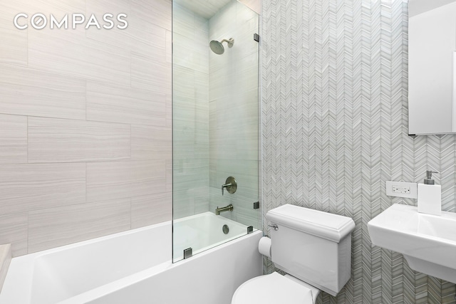 bathroom with a sink, tile walls, toilet, and shower / washtub combination