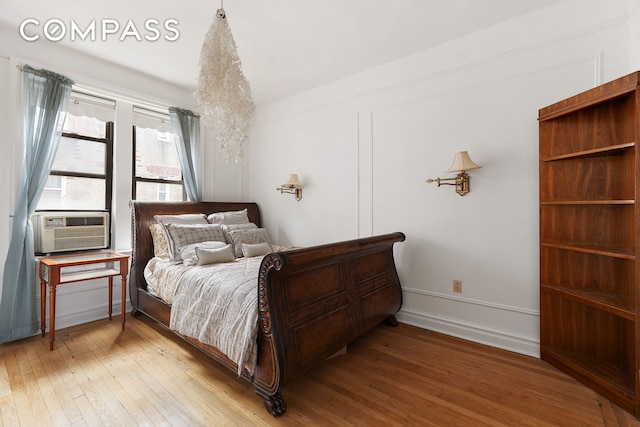 bedroom featuring a decorative wall, cooling unit, baseboards, and wood-type flooring