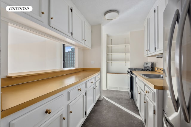 kitchen with concrete flooring, stainless steel appliances, a sink, white cabinetry, and light countertops