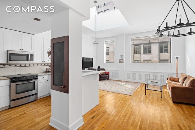 kitchen featuring stainless steel appliances, open floor plan, a chandelier, light wood-style flooring, and white cabinetry