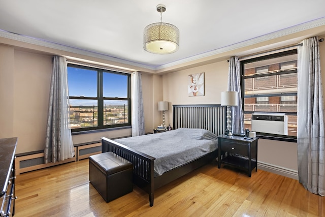 bedroom featuring light hardwood / wood-style floors, baseboard heating, and crown molding