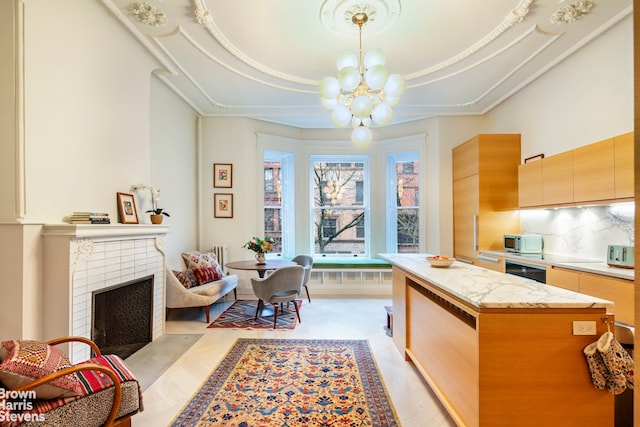 kitchen with a tiled fireplace, a kitchen island, a tray ceiling, a chandelier, and backsplash