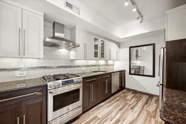 kitchen with visible vents, decorative backsplash, stainless steel appliances, wall chimney range hood, and a sink