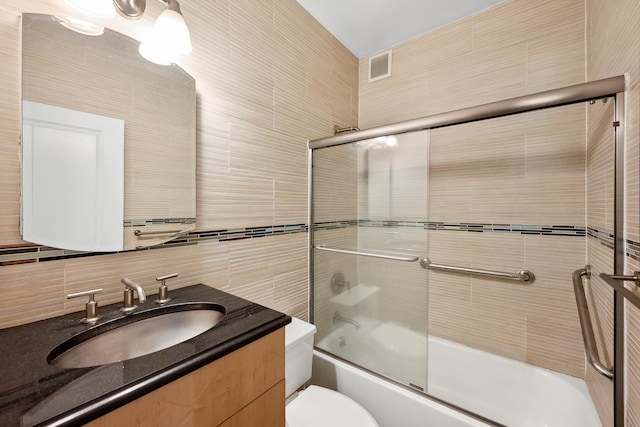 bathroom featuring visible vents, decorative backsplash, toilet, combined bath / shower with glass door, and vanity