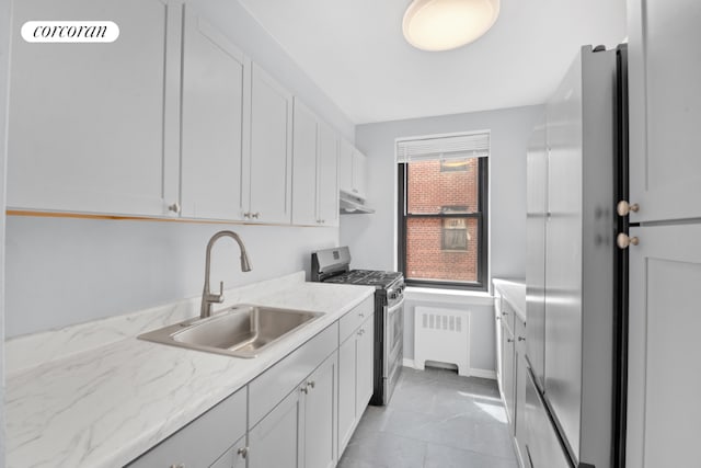 kitchen with radiator heating unit, gas stove, white cabinetry, sink, and light stone counters