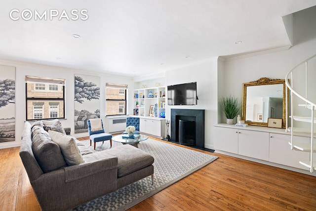 living room with a fireplace with flush hearth, light wood finished floors, and ornamental molding