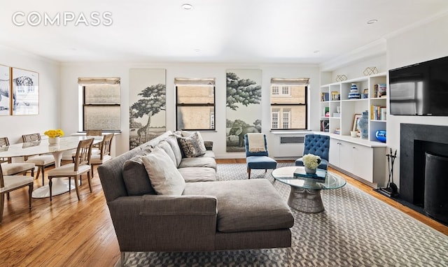 living room with crown molding, light wood-type flooring, a fireplace, and a healthy amount of sunlight