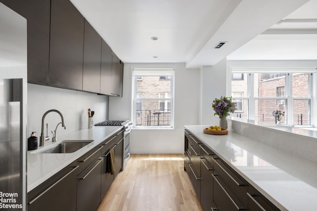 kitchen featuring light wood-type flooring, light stone countertops, sink, and stainless steel range with gas stovetop