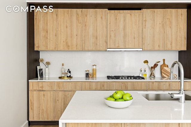 kitchen featuring light brown cabinetry, a sink, light countertops, black gas cooktop, and under cabinet range hood