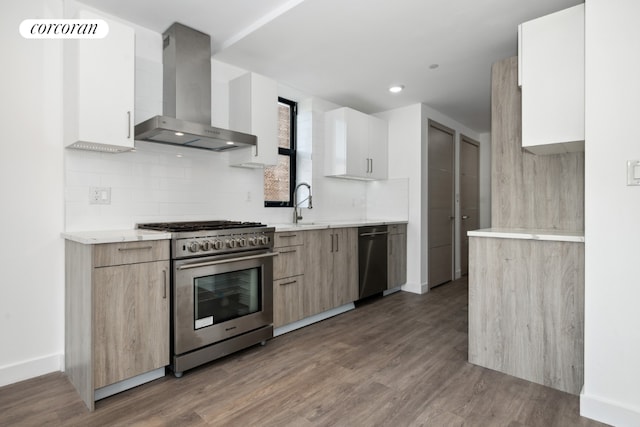 kitchen featuring white cabinets, wall chimney range hood, wood-type flooring, backsplash, and high end stainless steel range oven