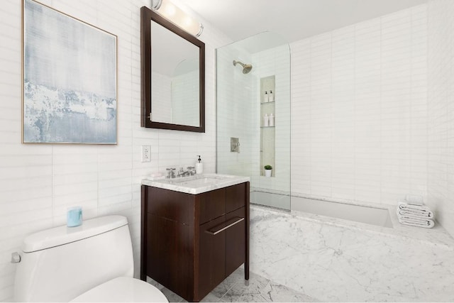 full bathroom featuring toilet, tiled shower / bath, tile walls, and vanity