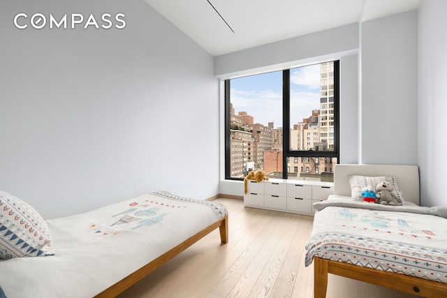 bedroom with lofted ceiling, light wood-style floors, and a city view