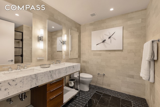 full bath featuring toilet, visible vents, a sink, and tile walls