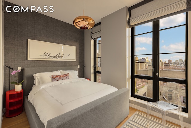 bedroom featuring an accent wall, wood finished floors, baseboards, a view of city, and wallpapered walls