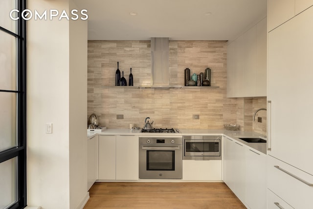 kitchen with wall chimney range hood, appliances with stainless steel finishes, light countertops, and a sink