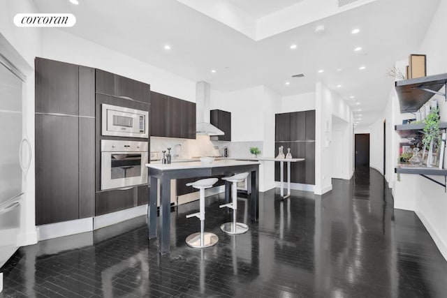 kitchen featuring wall chimney exhaust hood, dark brown cabinetry, sink, a breakfast bar area, and stainless steel appliances