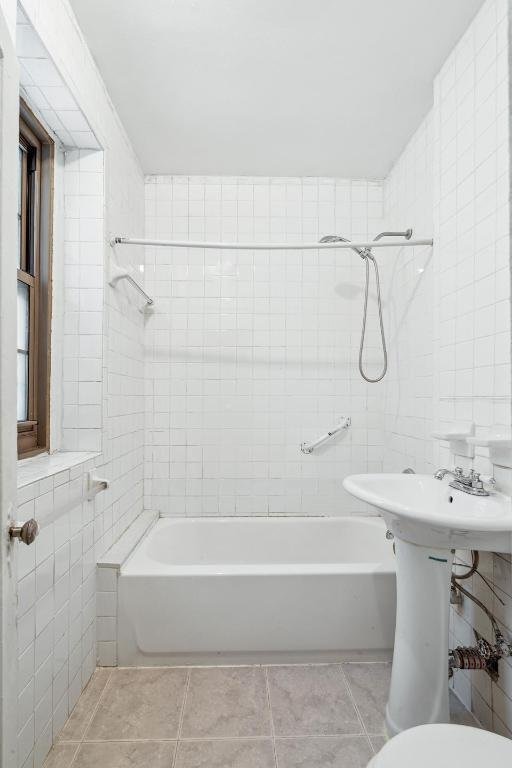 bathroom with tile patterned floors, toilet, tiled shower / bath combo, and tile walls