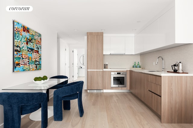 kitchen featuring white cabinetry, sink, oven, decorative backsplash, and light wood-type flooring