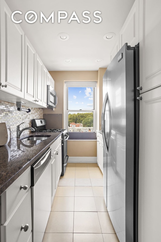 kitchen with light tile patterned floors, a sink, decorative backsplash, stainless steel appliances, and white cabinetry