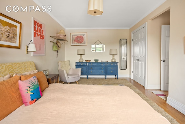 bedroom with a closet, crown molding, baseboards, and wood finished floors