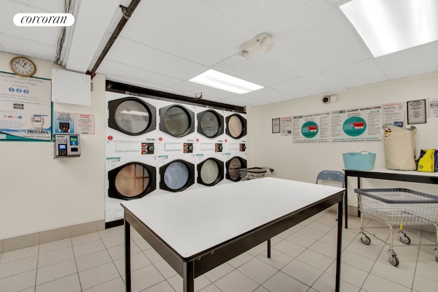 game room with a drop ceiling, stacked washer and clothes dryer, and light tile patterned flooring