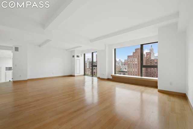 unfurnished room with beamed ceiling and light wood-type flooring