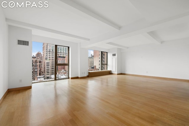 empty room with light hardwood / wood-style floors and beamed ceiling