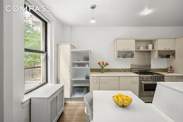 kitchen featuring light wood finished floors, light countertops, hanging light fixtures, cream cabinets, and stainless steel gas range oven