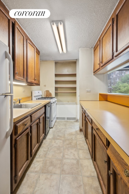 kitchen featuring sink, a textured ceiling, white gas range, and refrigerator