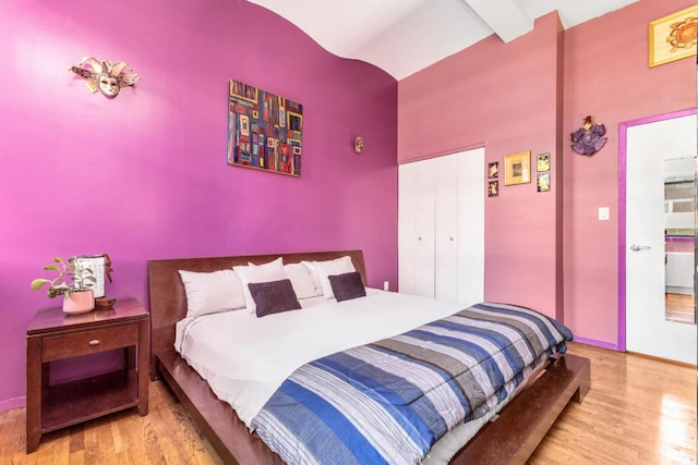 bedroom with a closet, light hardwood / wood-style floors, and beamed ceiling