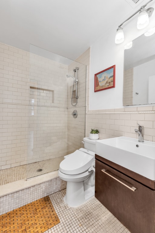 bathroom featuring toilet, tiled shower, tile patterned flooring, tile walls, and vanity