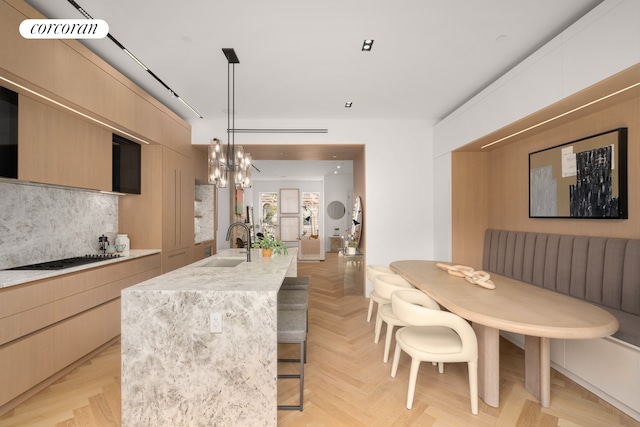 kitchen featuring decorative backsplash, an island with sink, modern cabinets, black stovetop, and a sink