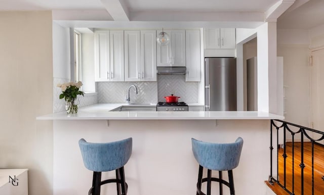 kitchen with white cabinetry, stove, stainless steel fridge, and a kitchen bar