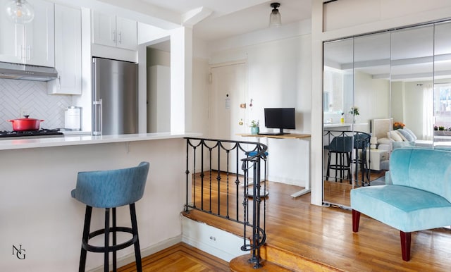 kitchen with a breakfast bar, open floor plan, white cabinetry, under cabinet range hood, and high end refrigerator