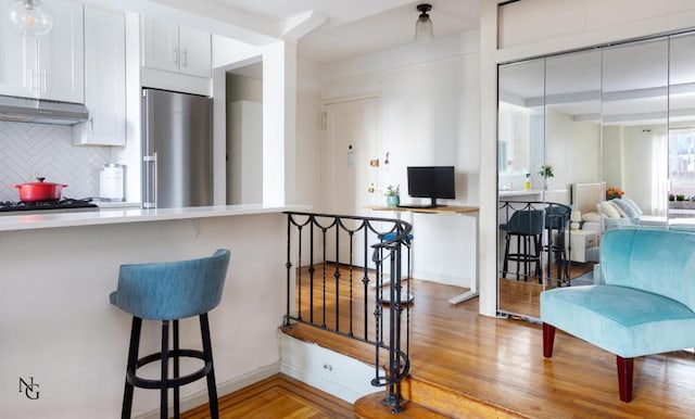 kitchen with white cabinetry, a breakfast bar area, backsplash, stainless steel built in fridge, and light wood-type flooring