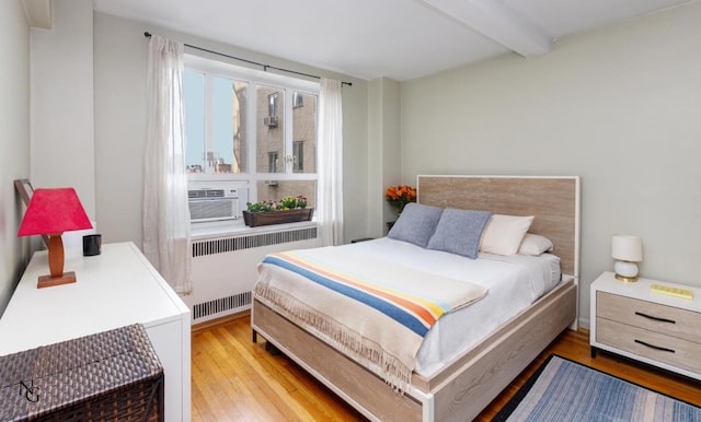 bedroom with beam ceiling, radiator heating unit, and light wood-type flooring