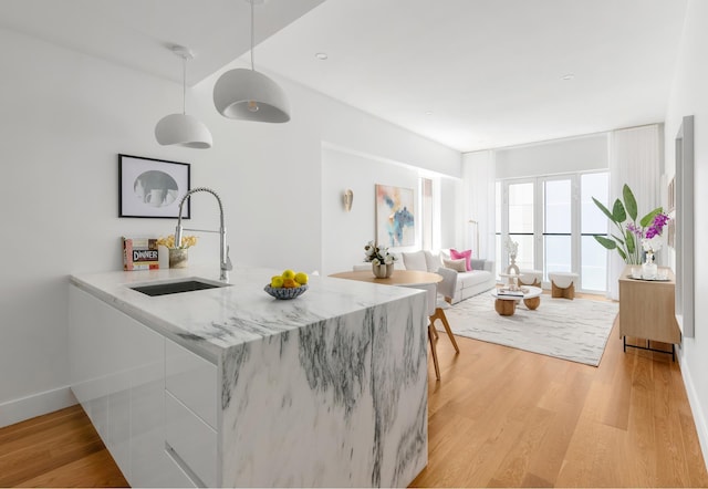 kitchen with white cabinets, a sink, light wood-style flooring, and light stone countertops