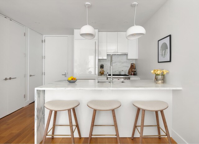 kitchen with light wood finished floors, tasteful backsplash, white cabinetry, and a breakfast bar