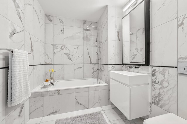 full bath with vanity, tiled shower / bath combo, tile walls, toilet, and marble finish floor