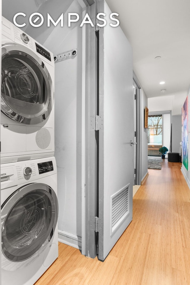 laundry area featuring laundry area, baseboards, visible vents, stacked washer and clothes dryer, and wood finished floors