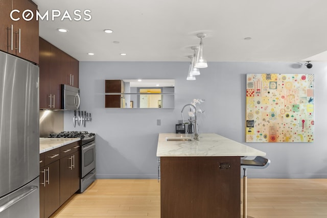 kitchen featuring stainless steel appliances, hanging light fixtures, light wood-style flooring, a sink, and dark brown cabinets