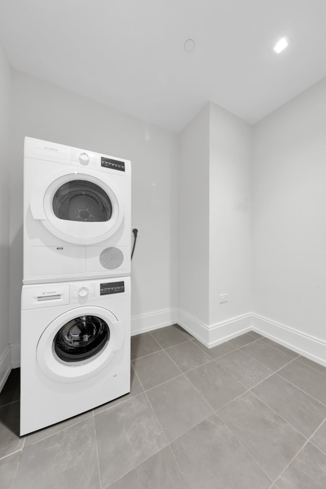 laundry area with laundry area, stacked washing maching and dryer, baseboards, and tile patterned flooring