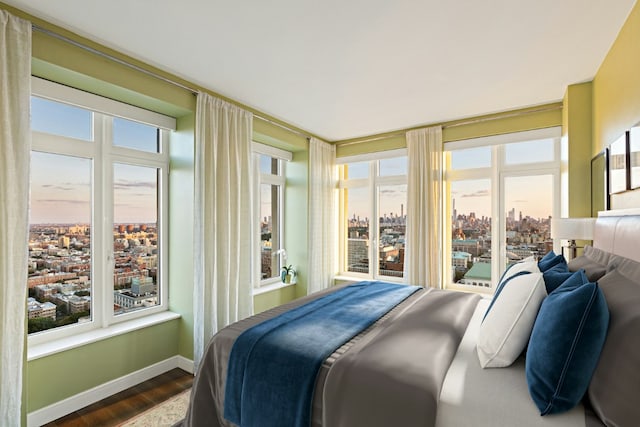 bedroom with a view of city, wood finished floors, and baseboards